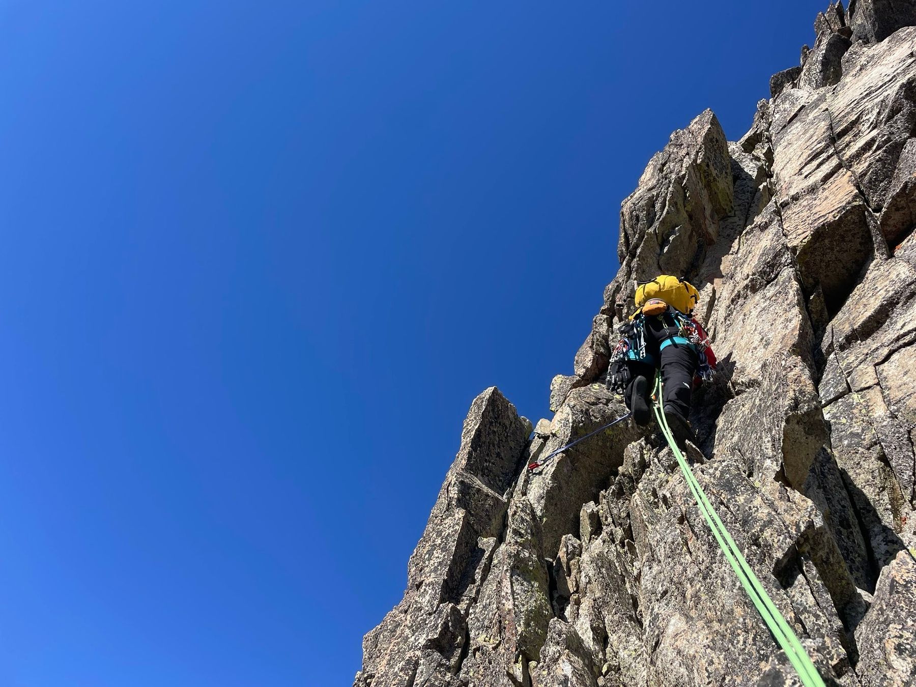 Un socio del club escala una arista de granito bajo un cielo azul intenso