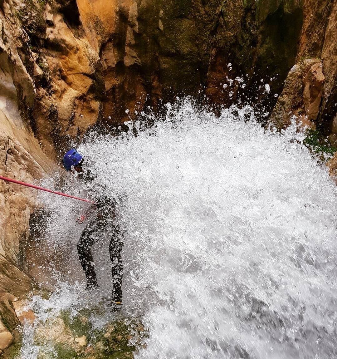 Un barranquista con casco azul rapela dentro de una cascada en un cañón